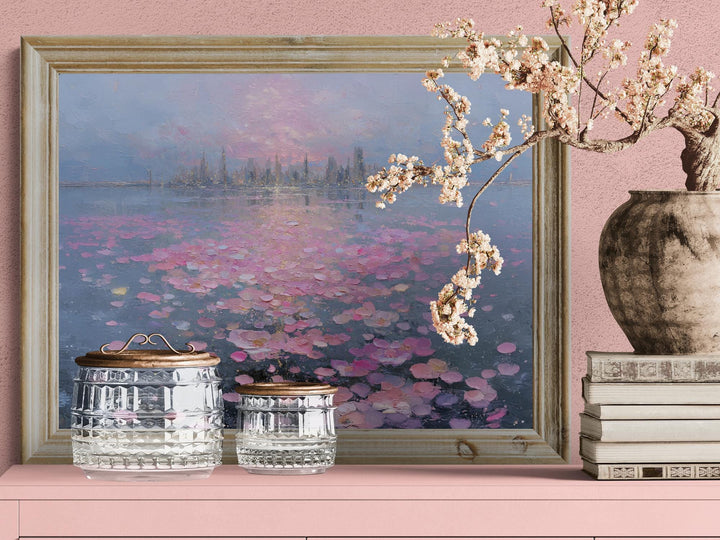 A romantic fantasy wall art depicting a glowing city and soft pink petals drifting across a mirrored lake at sunset.